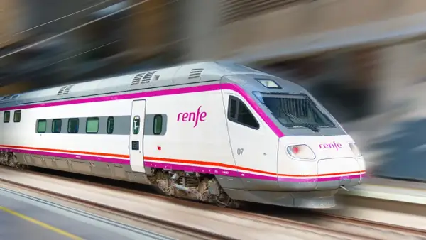 Ett modernt Renfe-tåg i Spanien susar fram längs spåren, med sina distinkta lila och vita färger.