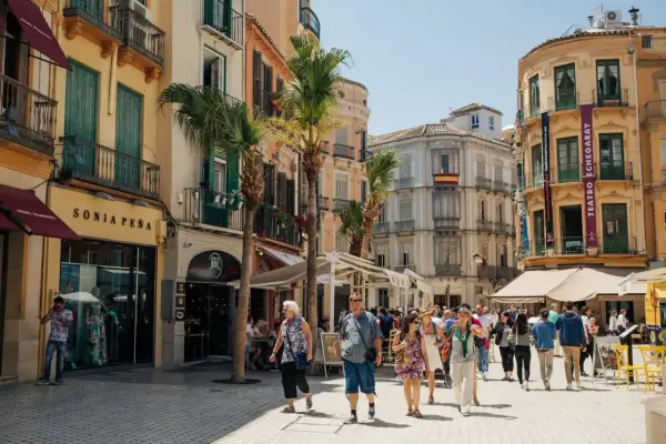 Folk promenerar på en solig gata i Malaga, kanske på väg till tågstationen för en resa till Stockholm.
