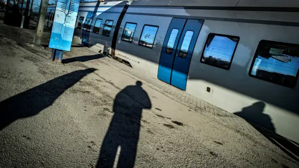 En skugga av en person står vid en tågvagn. En blå skylt med tåg linjer Stockholm syns bredvid.