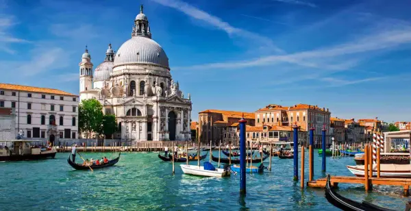 En gondol färdas på Venedigs kanaler framför den ståtliga kyrkan Santa Maria della Salute. En perfekt dag för en resa med tåg till Venedig.
